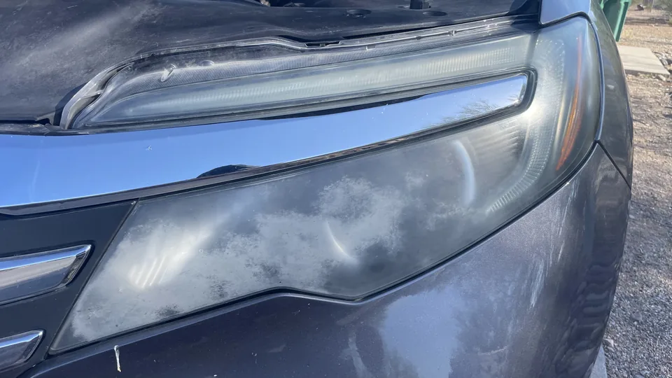 Before view of a headlight lens with visible haze or clouding and partly obscured internal lamp elements.